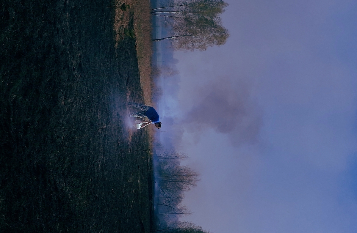Дата створення: 20.05.2025 Місце: село Соснівка. Країна: Україна. Тема: Вогняний Великдень. Опис: На фото зображена жителька села, що тушить залишки вогню водою з відра.