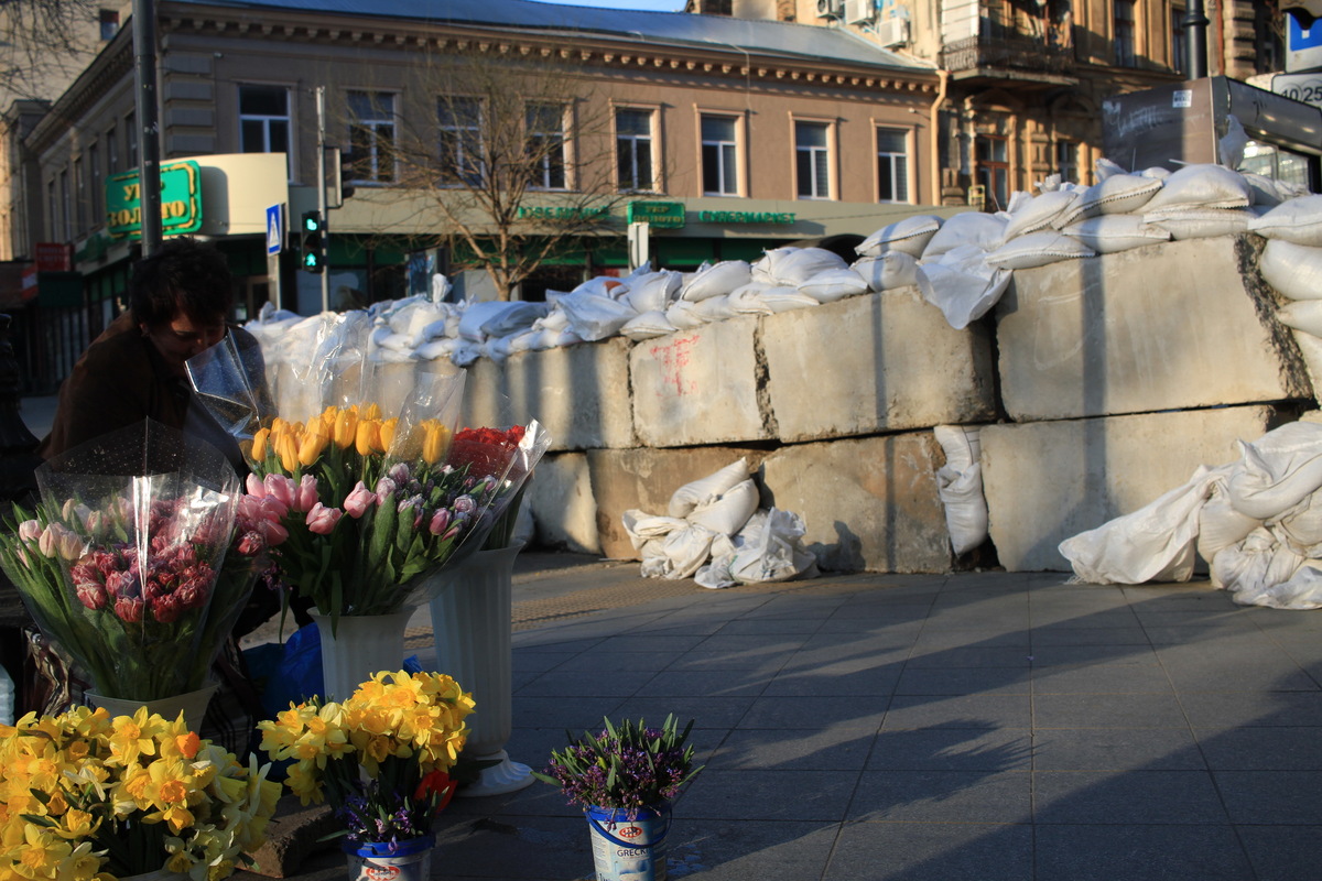 A woman sells flowers against the backdrop of concrete barricades in Odesa